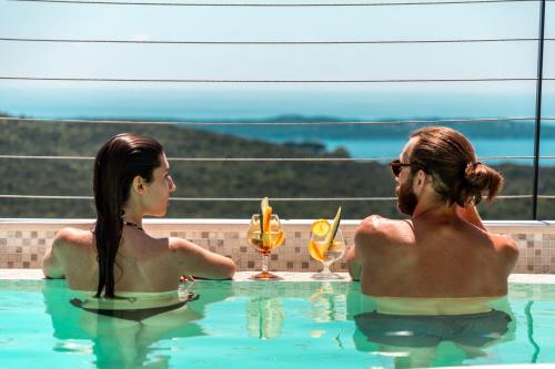 Dos personas sentadas en una piscina con bebidas en Luxury Holidays & Events - Villa Diva - Montenegro, en Klinci