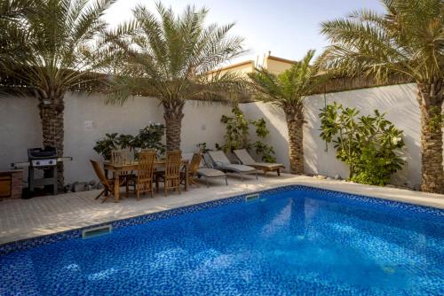 a swimming pool with a table and chairs and palm trees at Dar 66 Pool Chalets with Jacuzzi in Ras al Khaimah