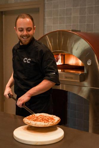 a man is putting a pizza into an oven at Cook's Club Corfu - Adults Only in Gouvia