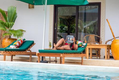 a woman laying on a raft reading a book next to a pool at Daima Villas in Jambiani