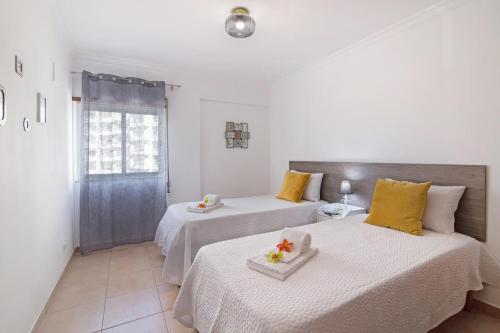 Duas camas num quarto branco com almofadas amarelas em Apartamento Sunlight by Sunnyway em Albufeira