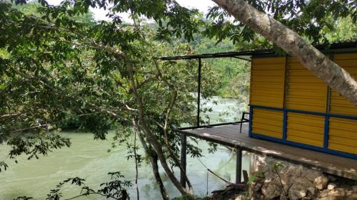 una casa junto al agua con un árbol en Room in Cabin - Rafting Hut by The River, en Lanquín