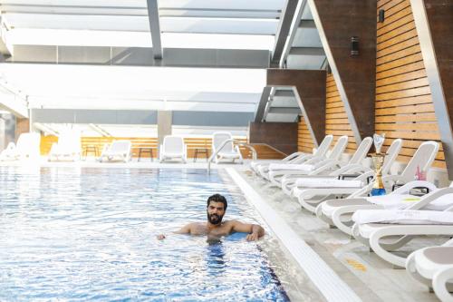 un uomo che nuota in una piscina con sedie di VIP Hotel Doha Qatar a Doha