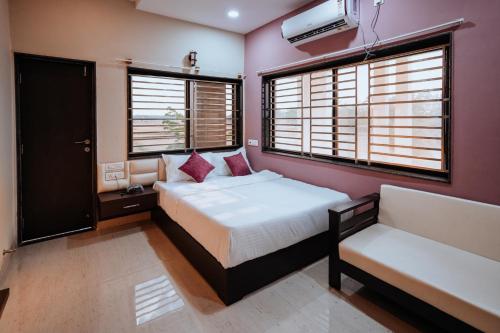 a bedroom with a bed and a chair and windows at Bajaj's Karwan Inn in Jagdalpur