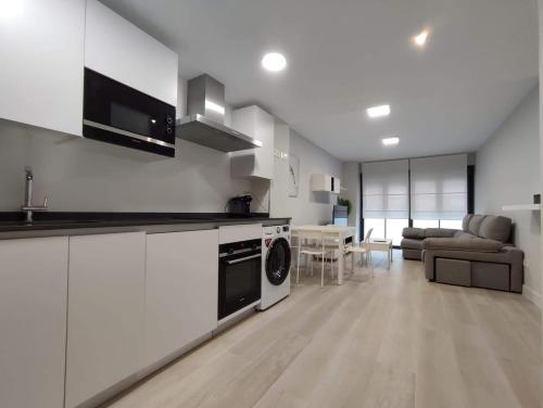 a kitchen with white cabinets and a living room at Apartamento LA ESTACIÓN con terraza in Gijón
