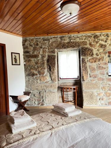 a bedroom with a stone wall with a bed and a window at CASA DE CAMPO BENFEITO in Campo Benfeito