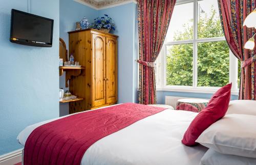 a bedroom with a bed with a red blanket and a window at Broadlands Guest House in Stratford-upon-Avon