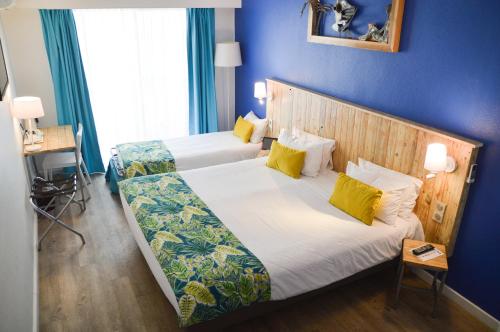 a hotel room with two beds and a blue wall at Hôtel Le Grand Bleu in Saint-Gilles les Bains