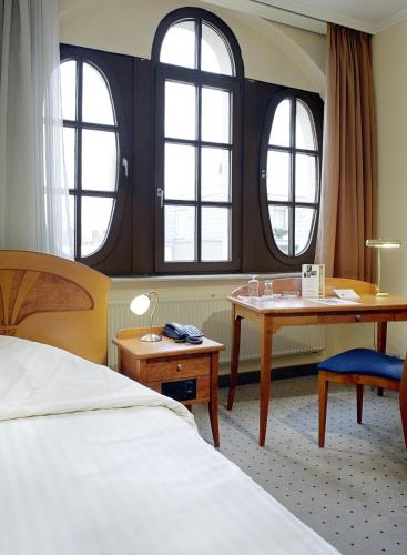 a hotel room with a bed and a desk and windows at Tryp by Wyndham Kassel City Centre in Kassel