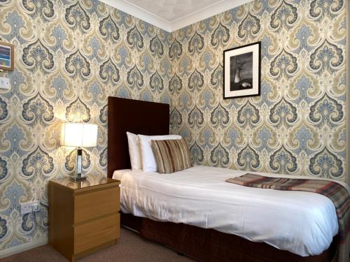 a bedroom with a bed and a lamp and wallpaper at Virginia Court Hotel in Cromer