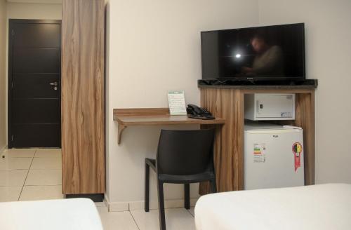 a room with a television and a table and a refrigerator at Rede Andrade Vivaldi in Foz do Iguaçu