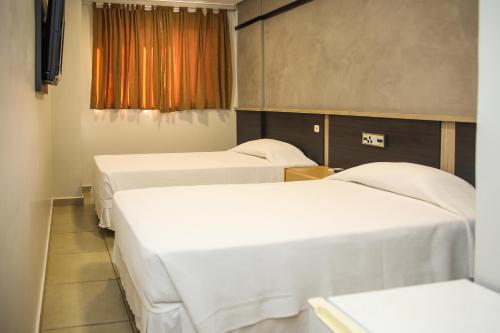 three beds in a room with white sheets at Rede Andrade Vivaldi in Foz do Iguaçu