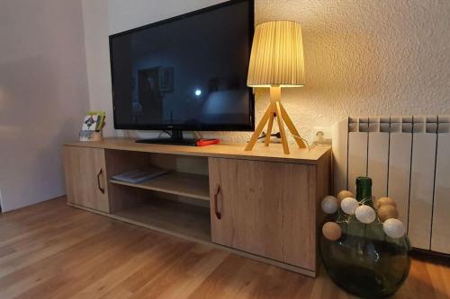 une télévision sur un meuble de divertissement en bois avec une lampe dans l'établissement Acollidor estudi amb encant nòrdic i amb parquing, al costat de Grandvalira, à Canillo