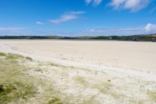 a large sandy beach with grass and a blue sky at 7A Ardroil in Uig