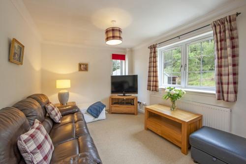 a living room with a leather couch and a television at Branter Lodge in Strachur