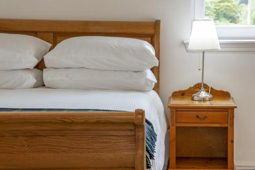 a bed with white pillows and a lamp on a table at Branter Lodge in Strachur
