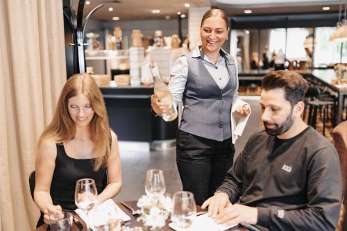a woman holding a glass of wine and two people sitting at a table at Holiday Inn Lübeck by IHG in Lübeck