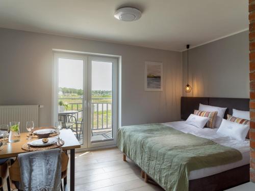 a bedroom with a bed and a table and a balcony at Vincent Apartamenty Darłówek in Darłowo