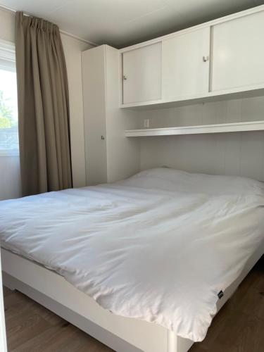 łóżko w pokoju z białymi szafkami i oknem w obiekcie Luxe chalet direct aan het water met strand w mieście Lith