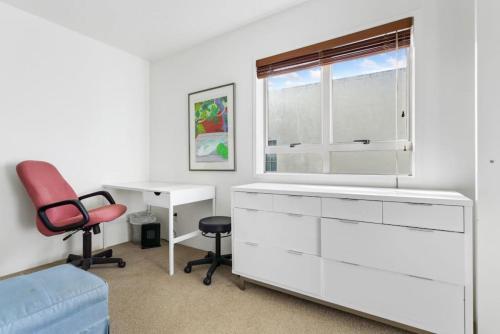 a white room with a red chair and a desk at CBD Spacious 3 Storey Terrace House with Courtyard in Auckland
