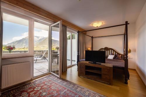a bedroom with a bed and a tv and a balcony at Hotel Finkennest - Panoramic Garden Resort in Schenna