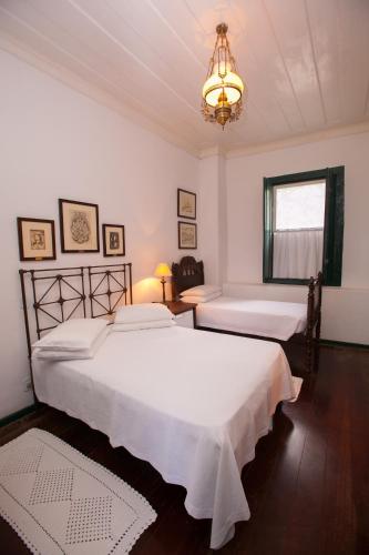 two beds in a white bedroom with a chandelier at Pousada da Marquesa in Paraty