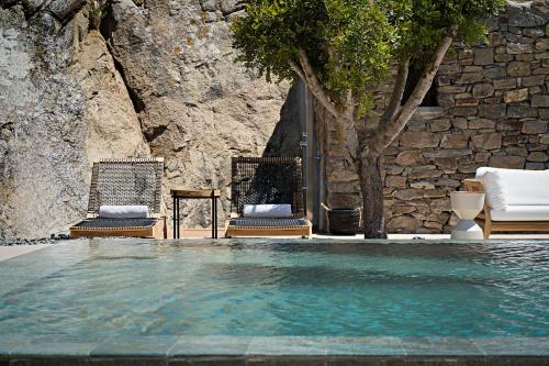 a swimming pool with two chairs and a stone wall at Cape Ftelia in Elia