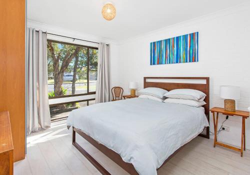 a white bedroom with a bed and a large window at Beach Breeze in Gerringong