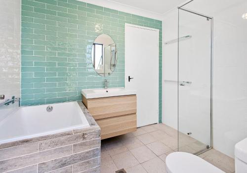 a bathroom with a tub and a sink and a mirror at Beach Breeze in Gerringong