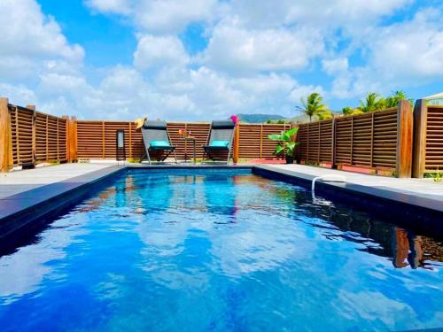 a swimming pool with blue water in front of a house at Villa Passion Cannelle de standing avec sa piscine vue mer in Les Trois-Îlets