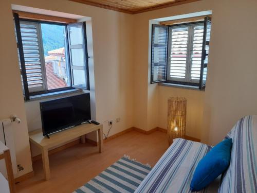 a room with a bed and a tv and windows at Casa das Neves in Manteigas