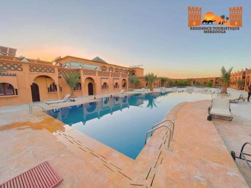 a large swimming pool in a building with blue water at Residence Touristique Merzouga in Merzouga