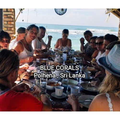 a group of people sitting around a table at the beach at Blue Corals Beach Bungalow in Madihe East