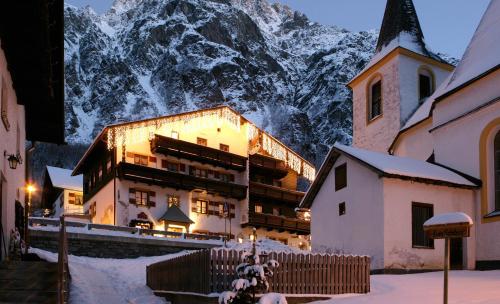 a building in the snow with a mountain in the background at Hotel Garni Kirchenwirt in Sankt Leonhard im Pitztal