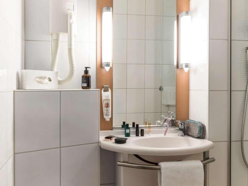 La salle de bains blanche est pourvue d'un lavabo et d'un miroir. dans l'établissement Ibis Sion, à Sion
