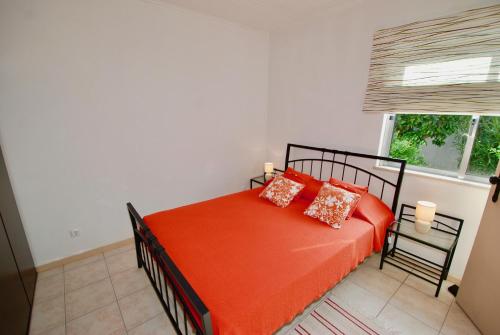 een slaapkamer met een bed met oranje lakens en een raam bij Laranjeira - House with private garden and pool in Alfeizerão