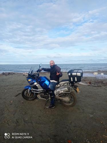 a man standing next to a blue motorcycle on the beach at HOSTAL BELLEZA TROPICAL in Moñitos