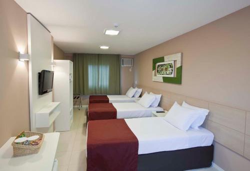 a hotel room with three beds and a television at Grande Hotel Itaguaí in Itaguaí