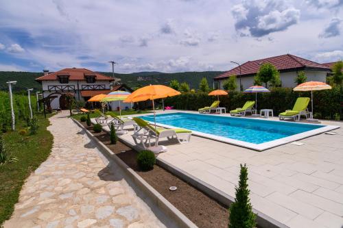 a swimming pool with chairs and umbrellas and a house at Holiday Home Bonum in Bihać
