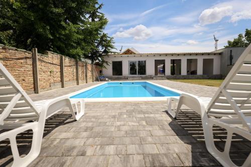 a swimming pool with two chairs and a house at Domaćin Komšijska Gostiona in Zrenjanin