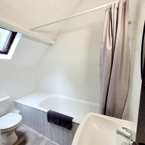 La salle de bains blanche est pourvue d'une baignoire et de toilettes. dans l'établissement Les Bruyères Rebecca, à Pleugueneuc