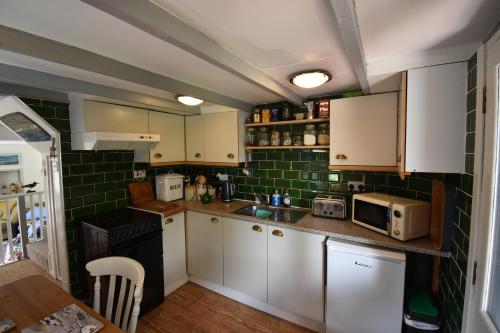 a small kitchen with white cabinets and green tiles at Yewtree Cottage - 'The Art House' and Garden in Hunters Quay