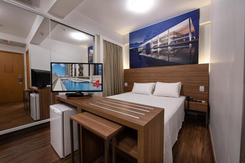 a bedroom with a bed and a desk with a monitor at S4 Hotel Águas Claras in Brasilia