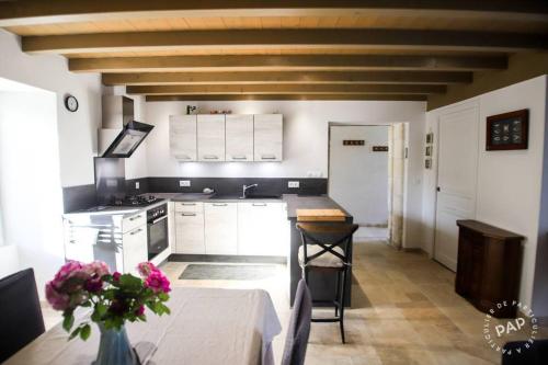una cocina con armarios blancos y una mesa con un jarrón de flores en la Belle Endormie, en Saint-Just