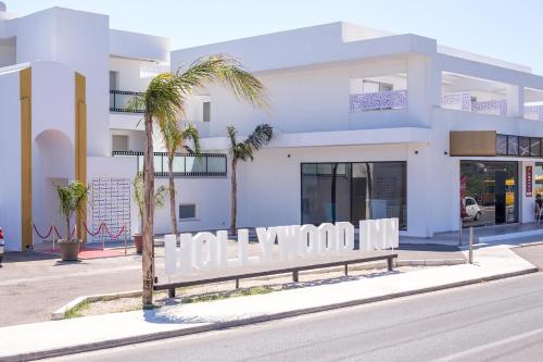 a white building with a palm tree in front of it at Hollywood Inn Faliraki - Adults Only in Faliraki