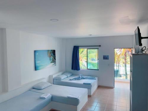 um quarto branco com 2 camas e uma janela em Blue Apartahotel em Coveñas