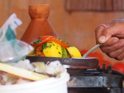 a person cooking food on a grill with a spoon at Dar Tifrouine in Lalla Takerkoust
