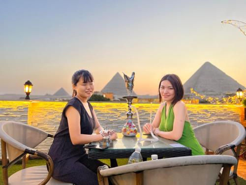 two women sitting at a table with pyramids in the background at Pyramids top success result in Cairo