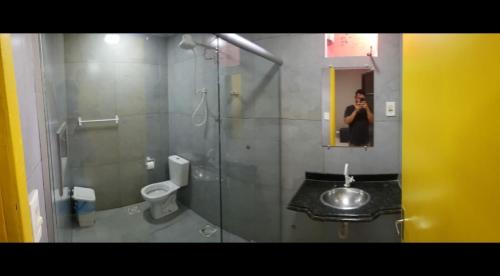 a woman taking a picture of a bathroom with a mirror at CITI COLIVING HOSTEL in Campo Grande