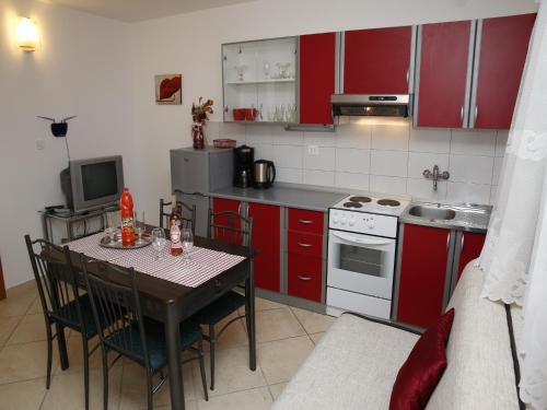 une cuisine avec des placards rouges et une table avec des chaises dans l'établissement Apartments M&R ŠPADINA, à Vodice